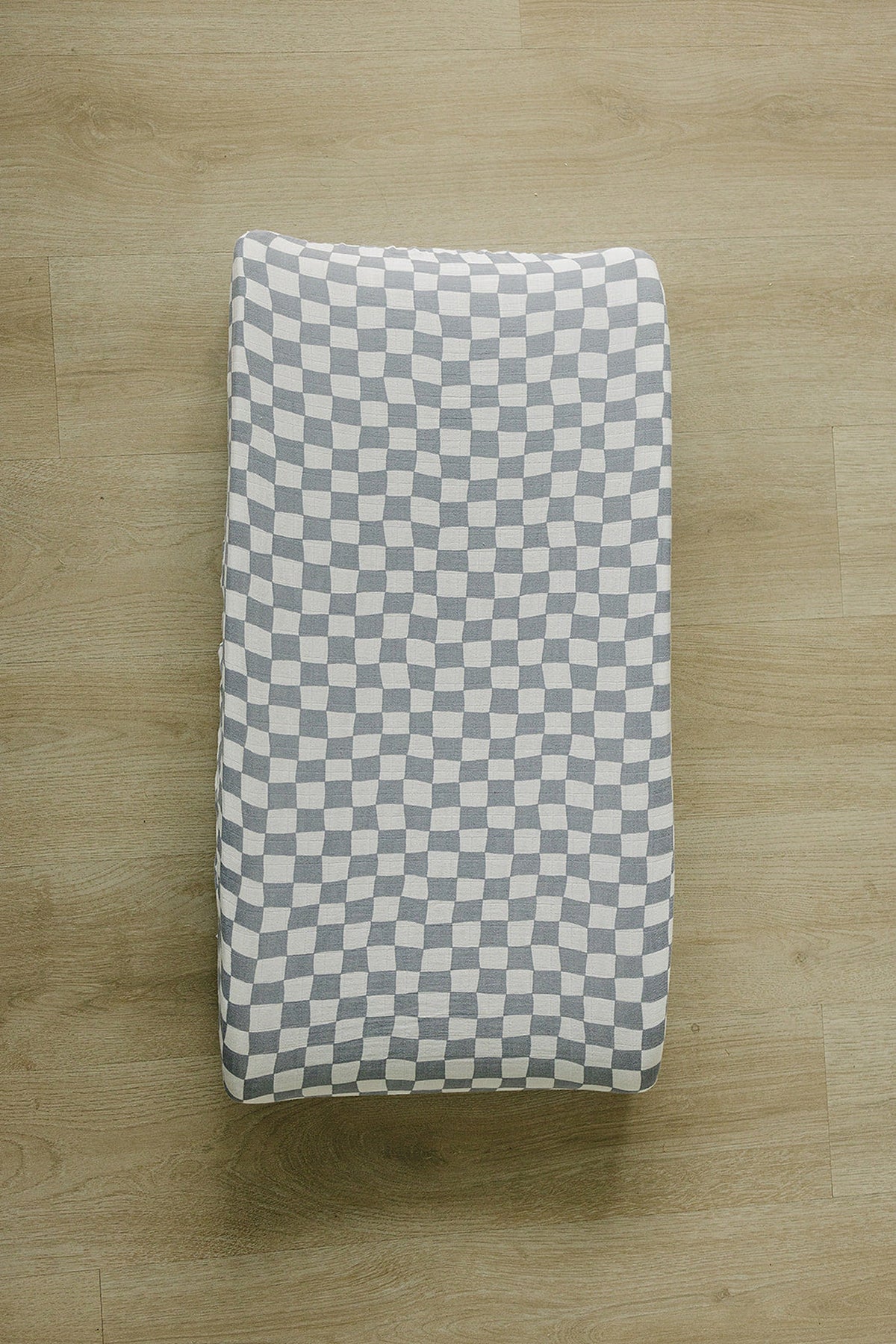 Dusty blue wavy checkered changing pad cover on a wooden floor, made of soft, breathable muslin fabric.