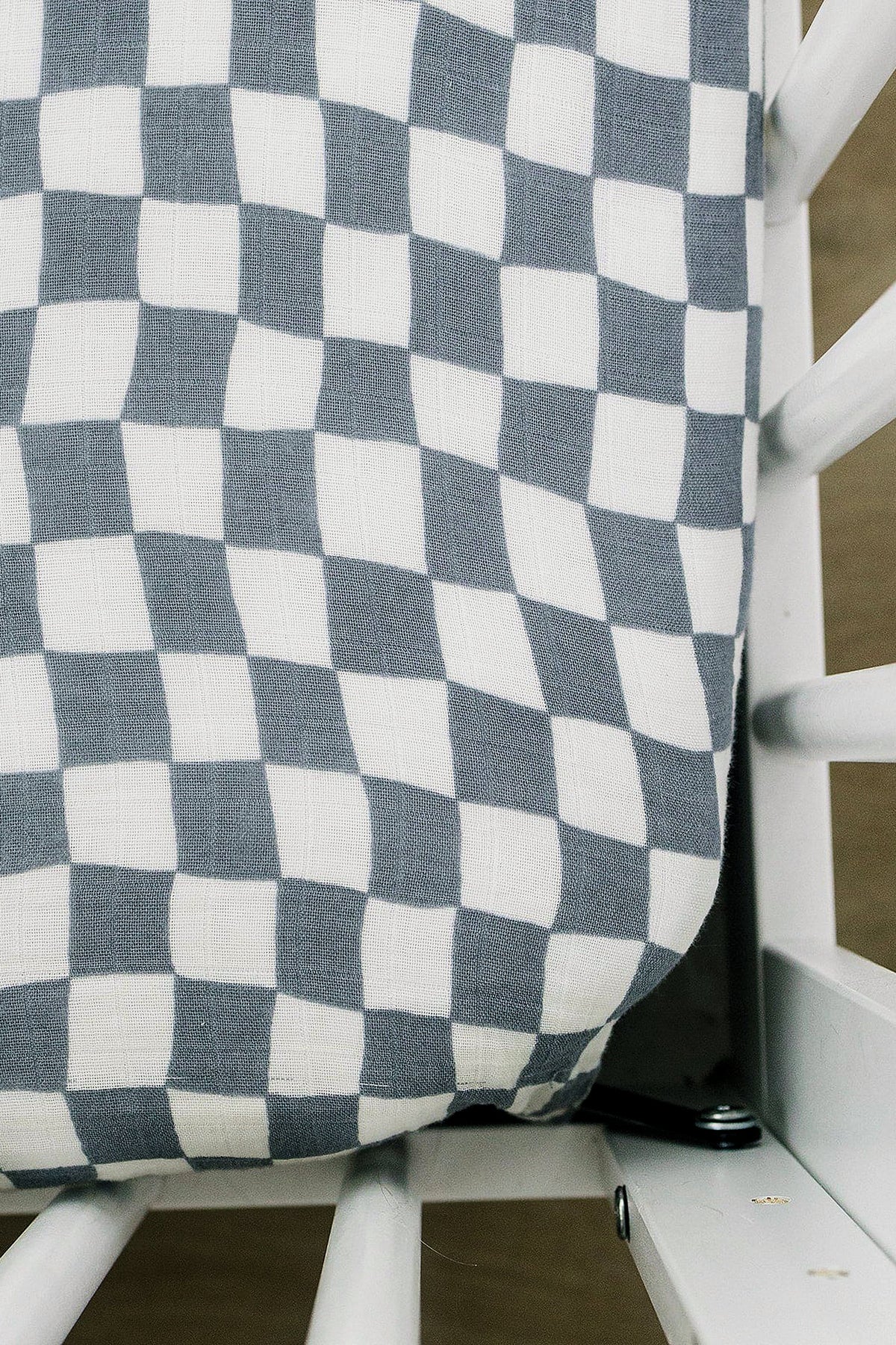 Dusty blue and white checkered muslin crib sheet on a white crib, showcasing a modern design.