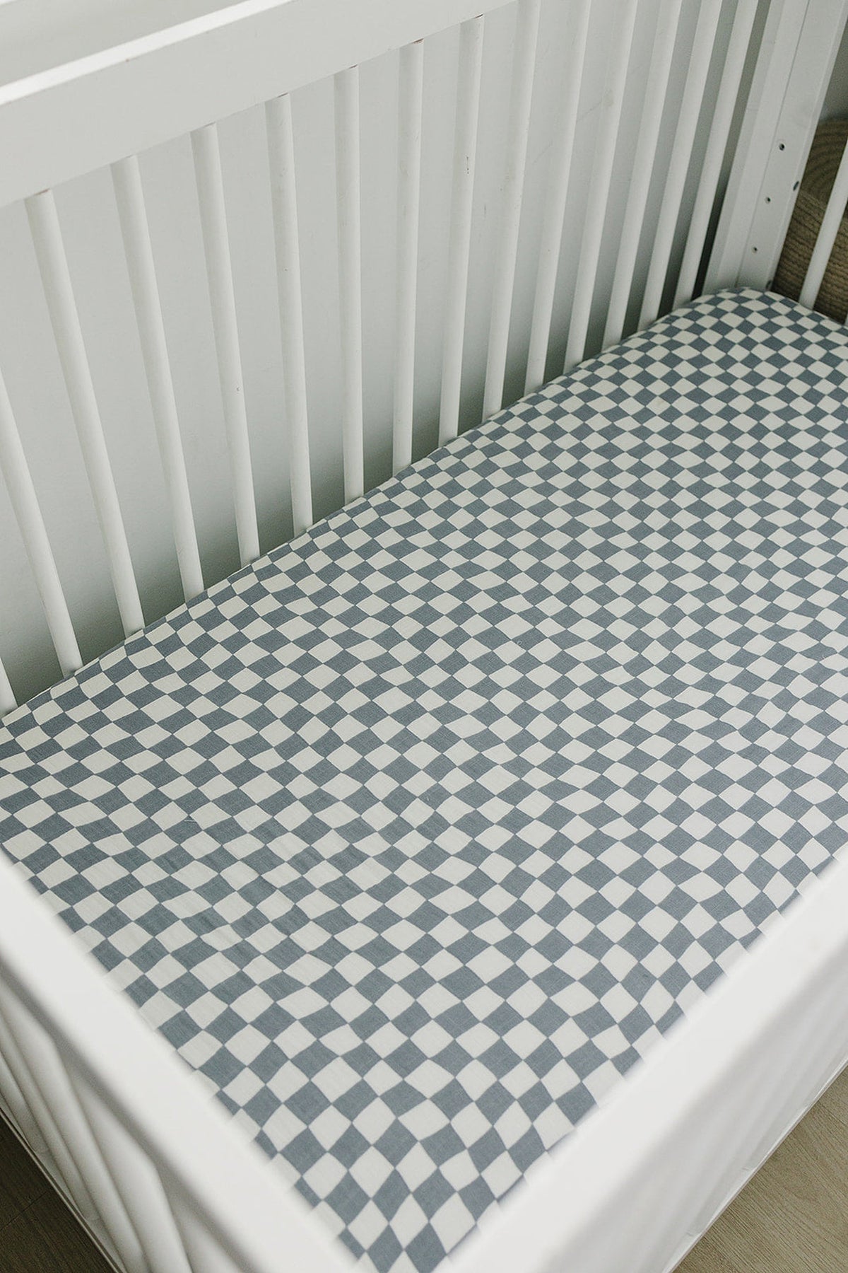 White crib with a dusty blue wavy checkered muslin sheet, providing a modern and cozy nursery look.