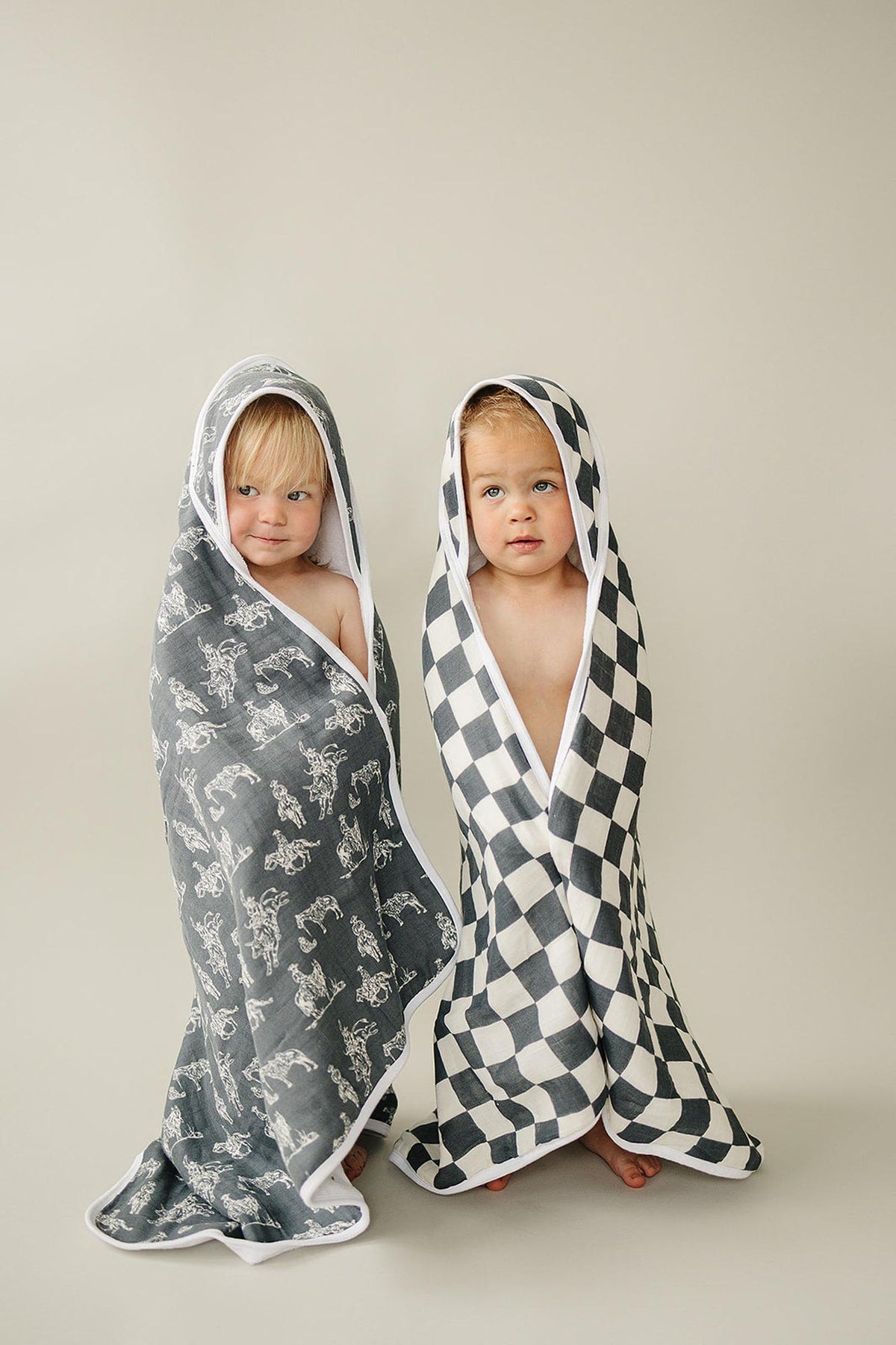 Two toddlers wrapped in hooded towels; one gray with white animals, the other black and white checkered.