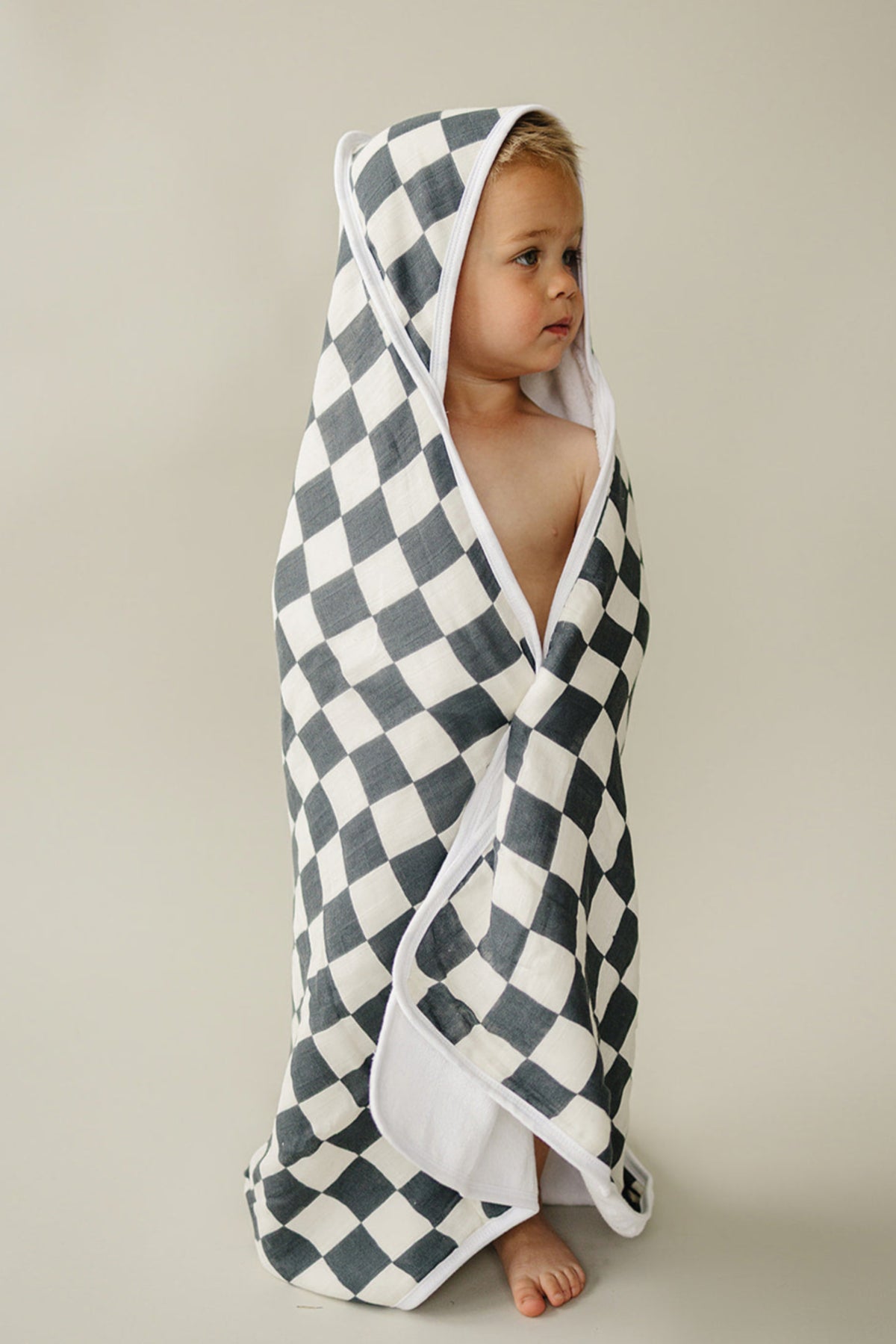 A child wrapped in a charcoal checkered hooded towel, made of soft cotton, standing against a neutral background.