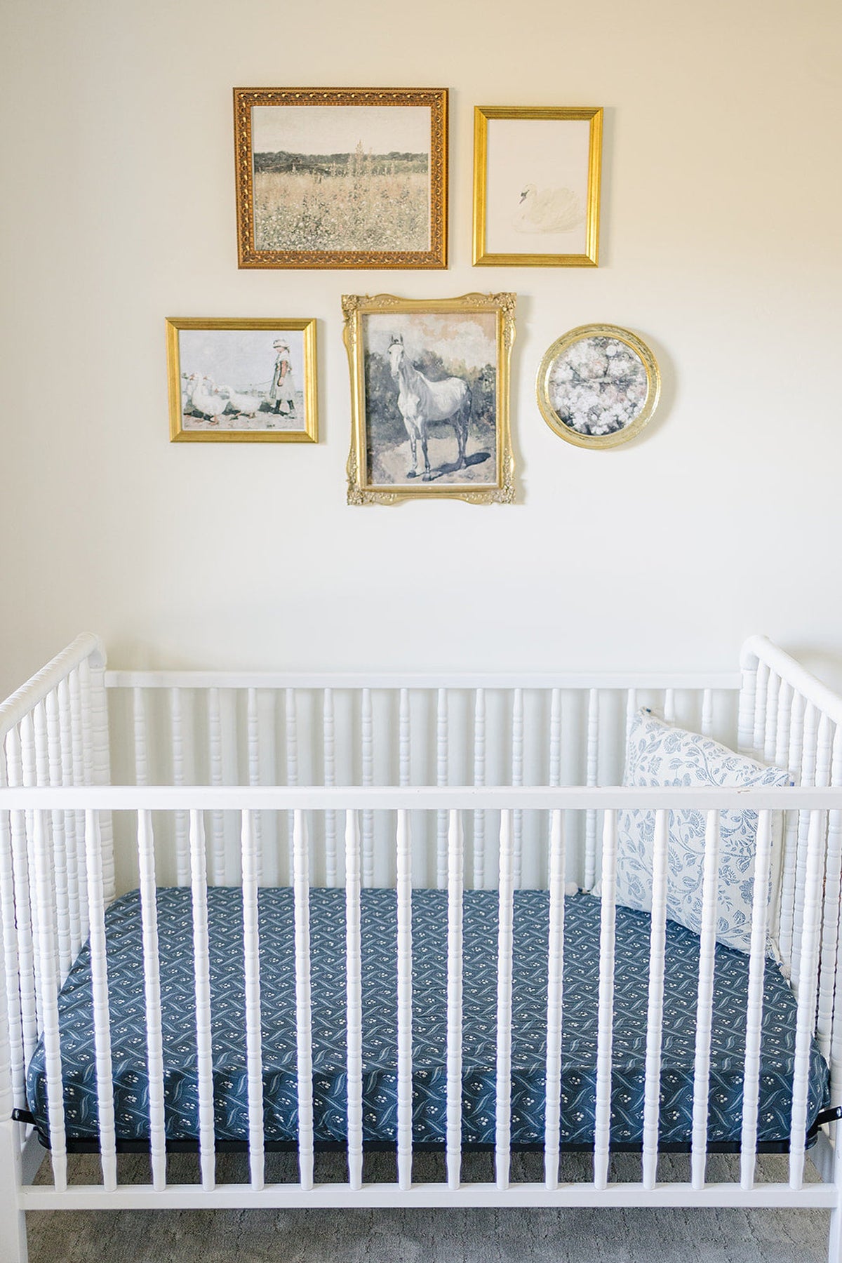 A white crib with a navy patterned sheet and a floral pillow, under framed artwork on the wall.