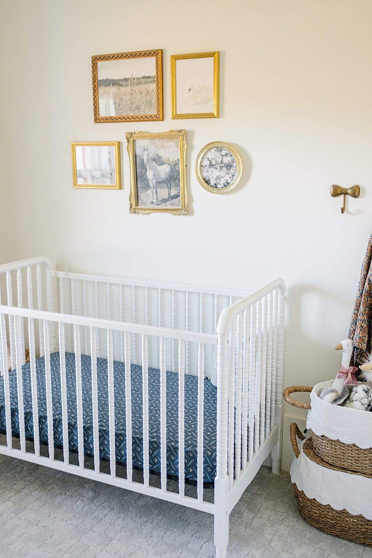 A white crib with a navy patterned sheet in a nursery, decorated with framed artwork and baskets.