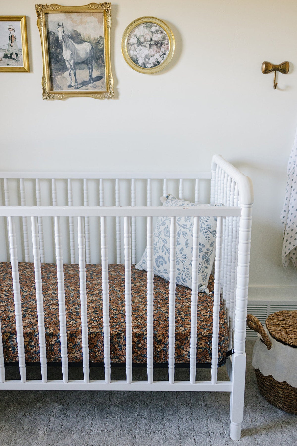 White crib with floral muslin sheet, blue patterned pillow, and decorative wall art in a cozy nursery.