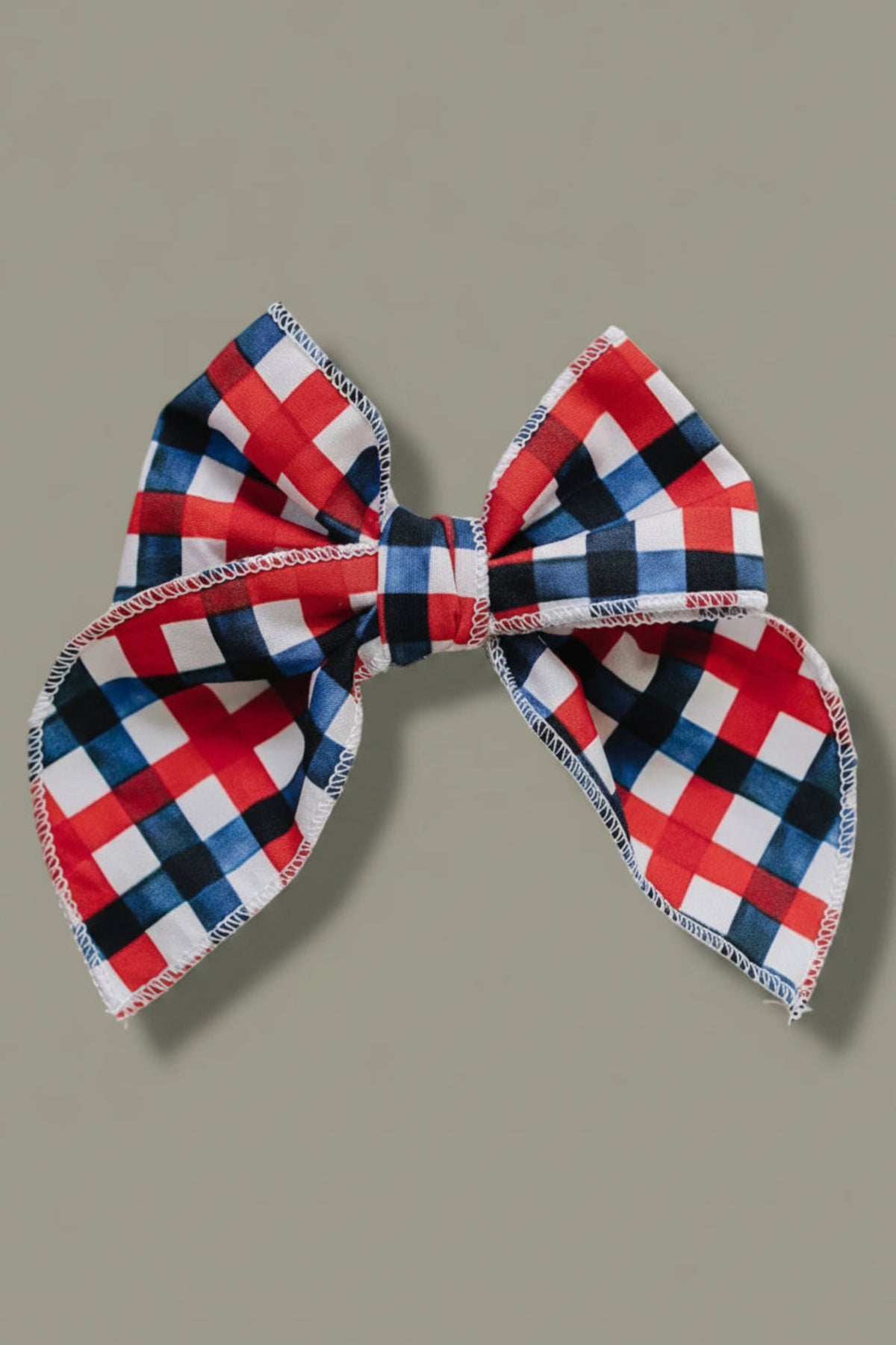 A large, handcrafted hair bow featuring a vibrant red, white, and blue plaid pattern. Made from 95% cotton and 5% spandex, its perfect for adding charm to any outfit.