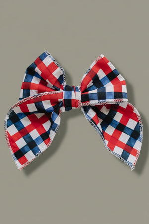 A large, handcrafted hair bow featuring a vibrant red, white, and blue plaid pattern. Made from 95% cotton and 5% spandex, its perfect for adding charm to any outfit.