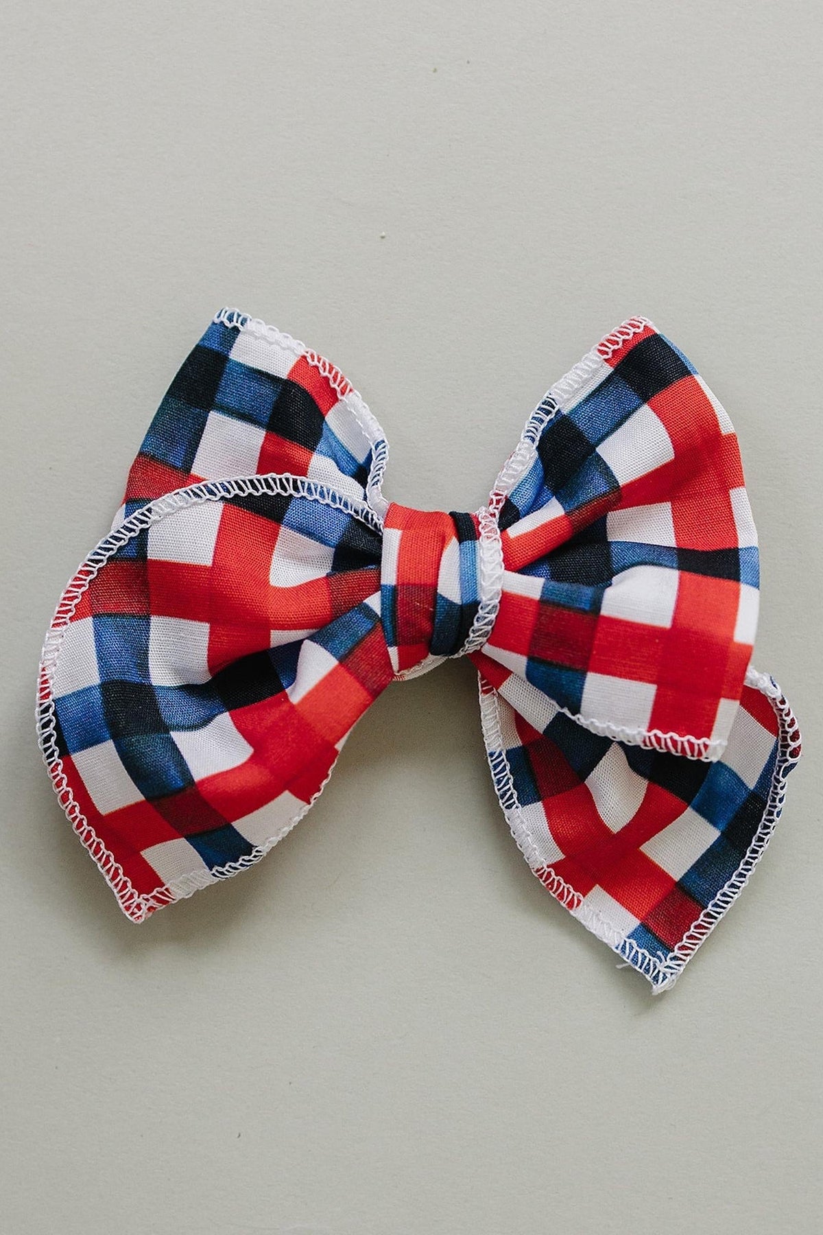A vibrant red, white, and blue plaid hair bow made from soft fabric. This handcrafted accessory is perfect for adding charm to outfits for children of all ages.