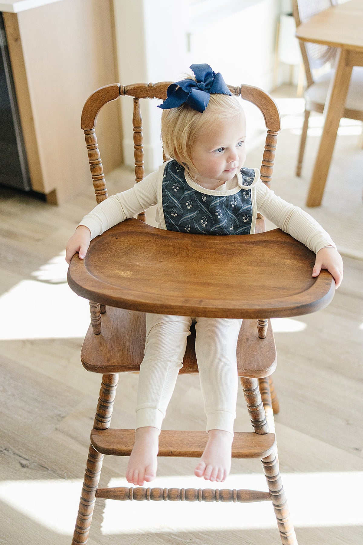 A toddler in a high chair wears a navy bib with a berry pattern and a matching hair bow.