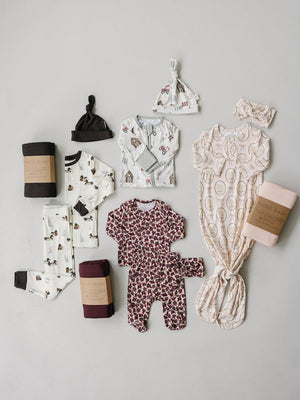 A flat lay displays a variety of baby and kids sleepwear, featuring ribbed bamboo fabric in soft colors and playful patterns, including pajamas, a sleep sack, and matching accessories.