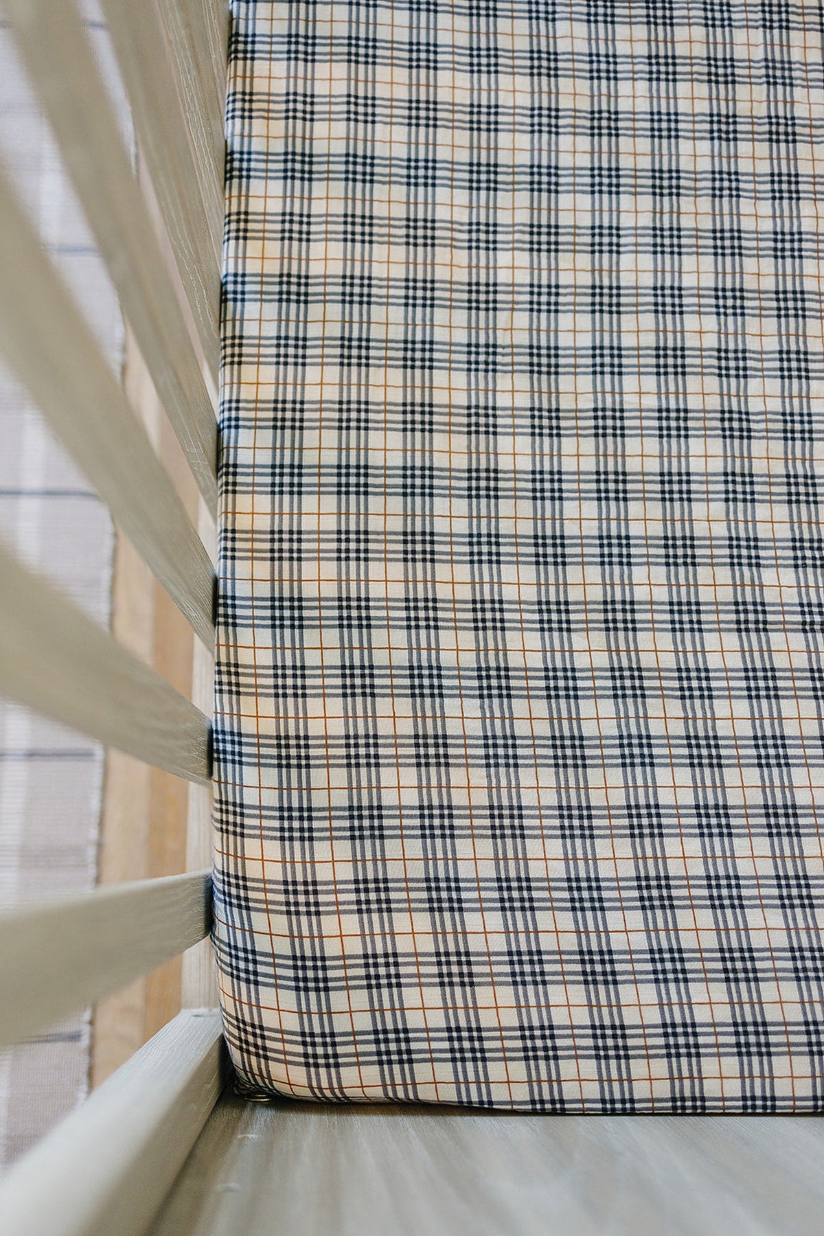 A crib with a vintage plaid muslin sheet in black and beige tones, showcasing a cozy, classic design.