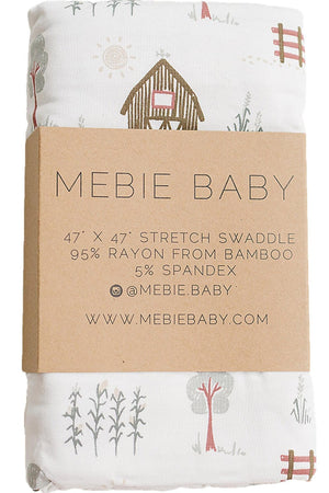 Mebie Babys 47 x 47 stretch swaddle features a soft bamboo fabric with whimsical farm-themed illustrations, including trees and a barn, perfect for stylish and eco-friendly swaddling.