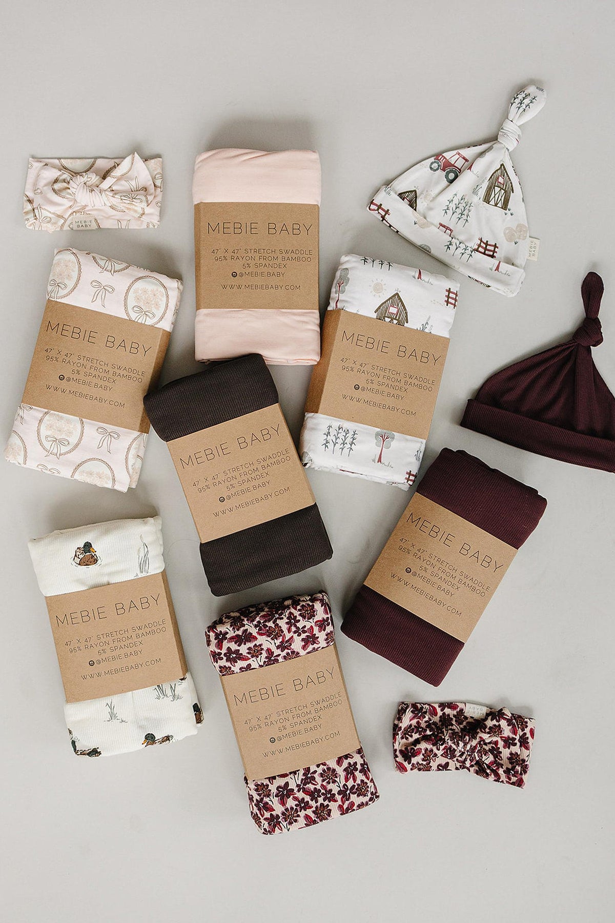 A flat lay arrangement of various baby essentials, including swaddles and hats in soft fabrics. The items feature neutral tones and whimsical patterns, showcasing Mebie Babys gentle, sustainable materials.