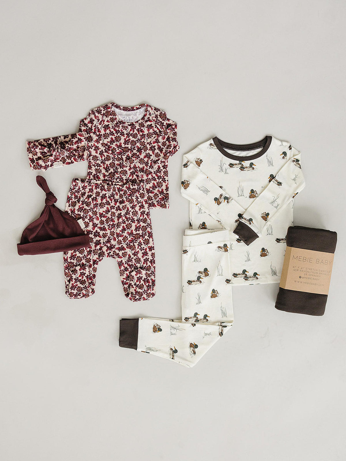 A cozy pajama set featuring a white top with duck illustrations and matching pants, alongside a floral onesie and a maroon hat. Made from soft, sustainable bamboo fabric for comfort.