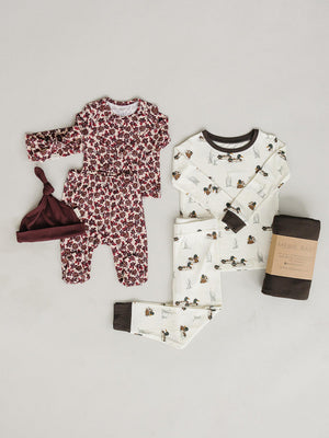 A cozy pajama set featuring a white top with duck illustrations and matching pants, alongside a floral onesie and a maroon hat. Made from soft, sustainable bamboo fabric for comfort.