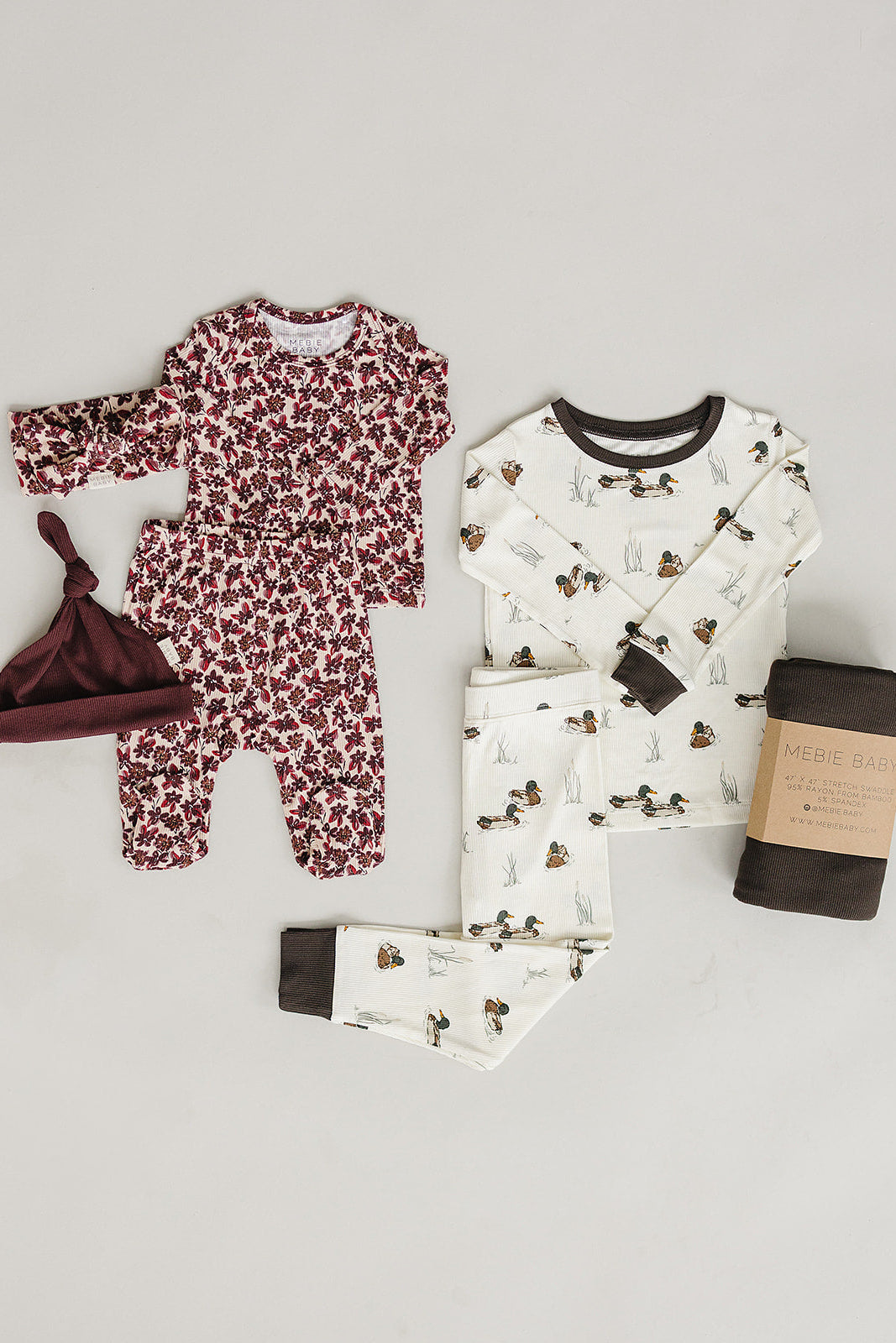 A soft, ribbed bamboo layette set featuring a floral romper, a matching hat, and a duck-patterned pajama set in cream and maroon, ideal for newborns and toddlers.