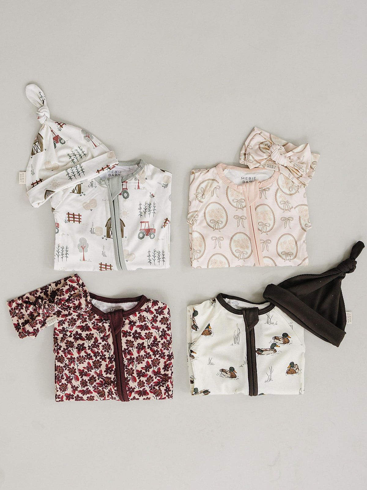 A collection of baby pajamas and hats displays various patterns, including floral and woodland themes. The pieces feature ribbed bamboo fabric, ensuring softness and comfort for infants.