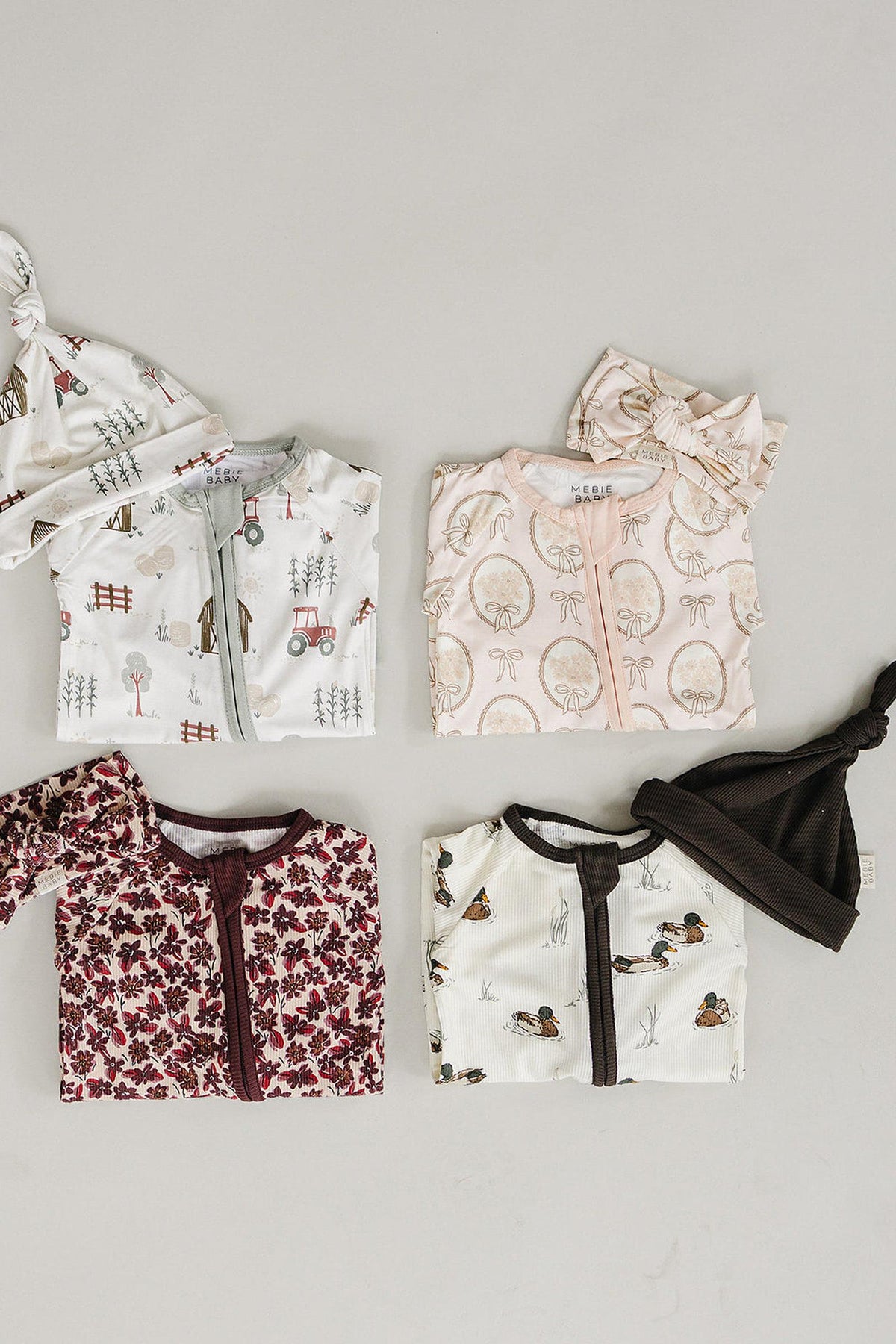 A flat lay displays four baby pajamas in soft bamboo fabric, featuring various whimsical prints, including tractors and mushrooms. Each pajama is paired with matching hats, emphasizing comfort and style.
