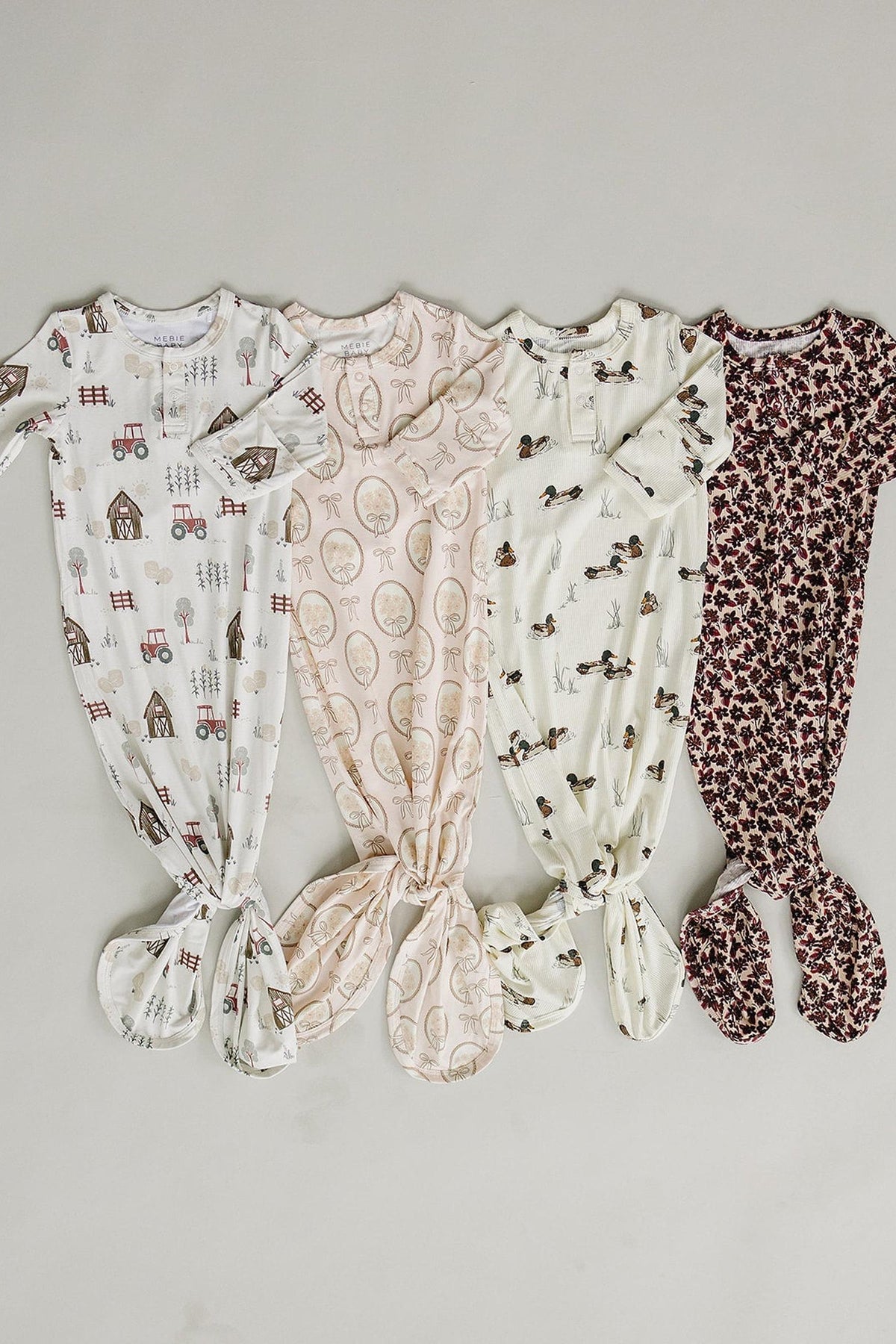 Four ribbed bamboo knot gowns in soft pastel colors, featuring playful patterns like tractors and animals, designed for babies. These eco-friendly garments offer comfort and easy diaper changes.
