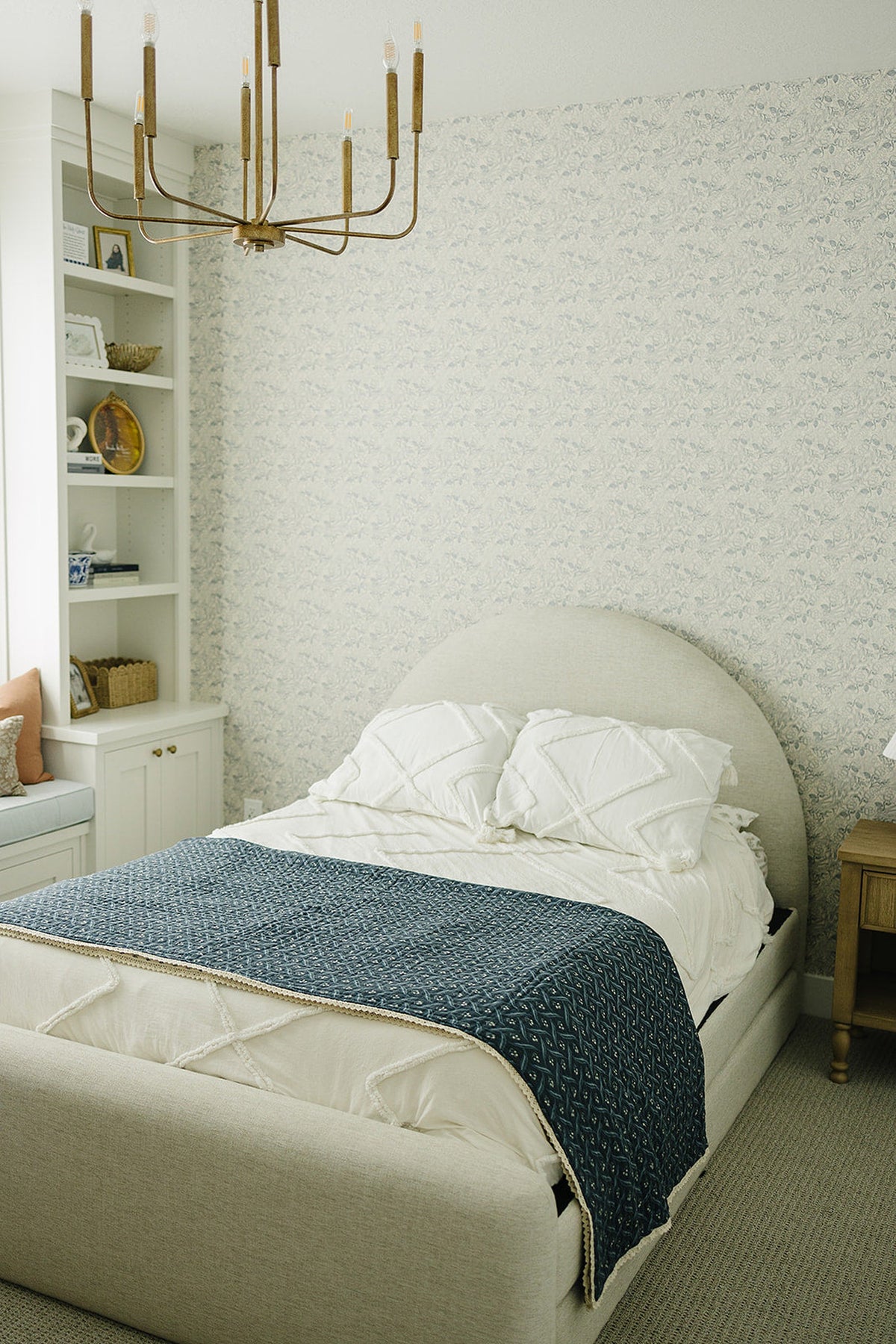 A cozy bedroom with a beige upholstered bed featuring a navy-patterned quilt and white textured pillows.