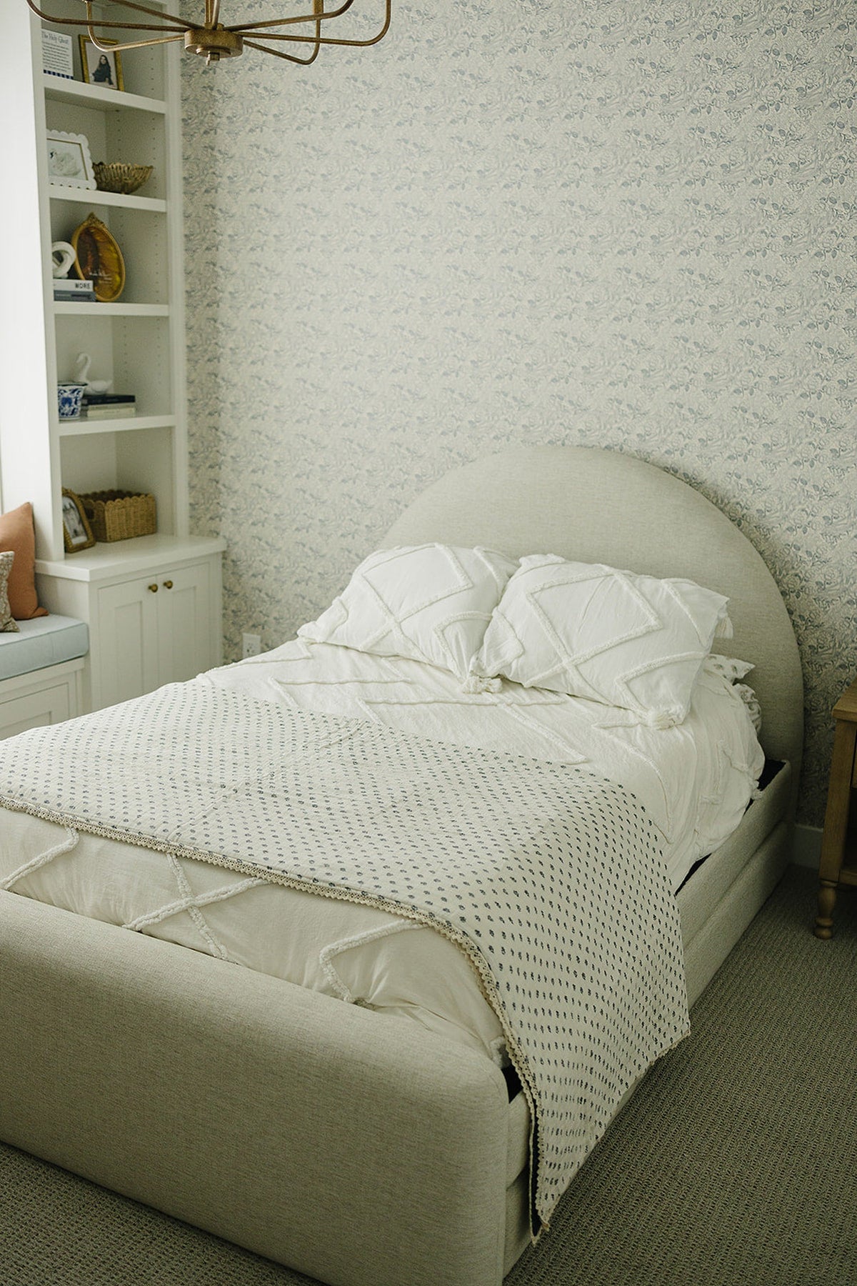 A cozy bedroom features a light beige upholstered bed with white bedding and a patterned quilt.