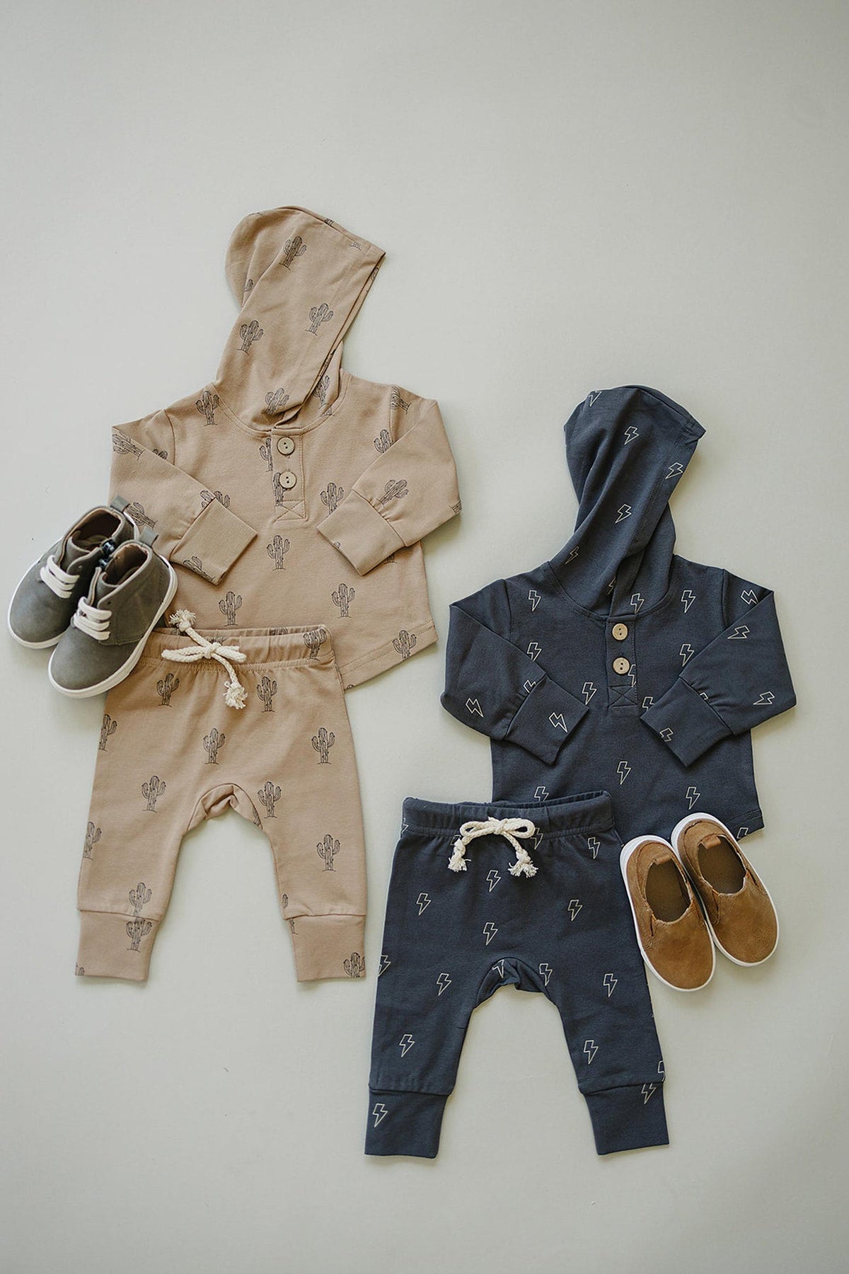 Two baby hooded sets, one beige with cactus print, one navy with lightning bolts, paired with shoes.