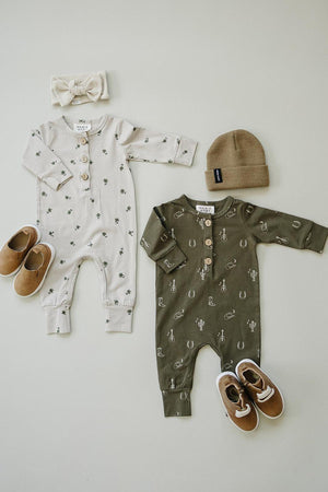 Two Mebie Baby rompers with western patterns, one cream and one olive green, paired with shoes and a beanie.