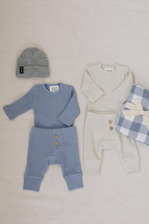 A dusty blue waffle knit baby set is displayed alongside a light gray version, both featuring long sleeves and button details.
