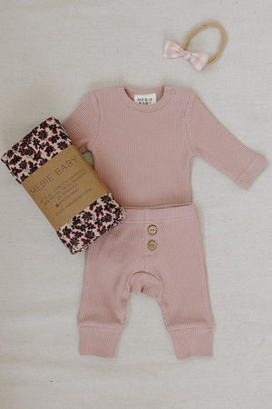 Dusty pink waffle knit cotton baby set featuring a long-sleeve bodysuit and relaxed fit pants, accompanied by a floral-patterned swaddle and a matching hair accessory. Perfect for comfort and style.