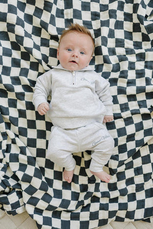 Baby wearing a grey quarter zip sweatshirt and pants with Good Vibes text, lying on a checkered blanket.