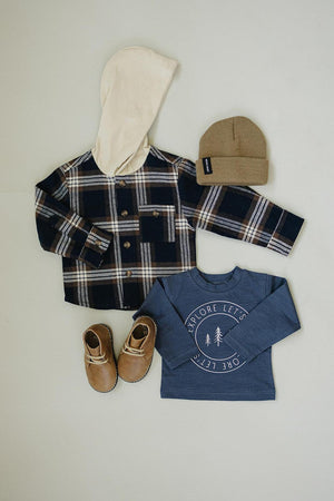 Plaid hooded button-up shirt with tan hood, blue graphic tee, brown boots, and a tan knit beanie.