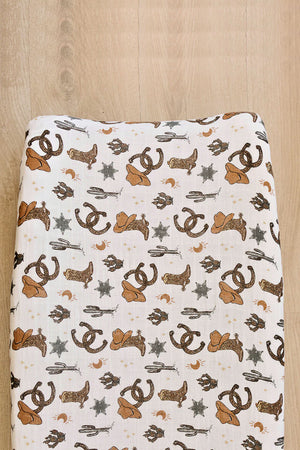 A muslin changing pad cover featuring a playful cowboy theme, showcasing brown hats, stars, and horseshoes on a light background. Made from 100% cotton, its soft and breathable for babies.