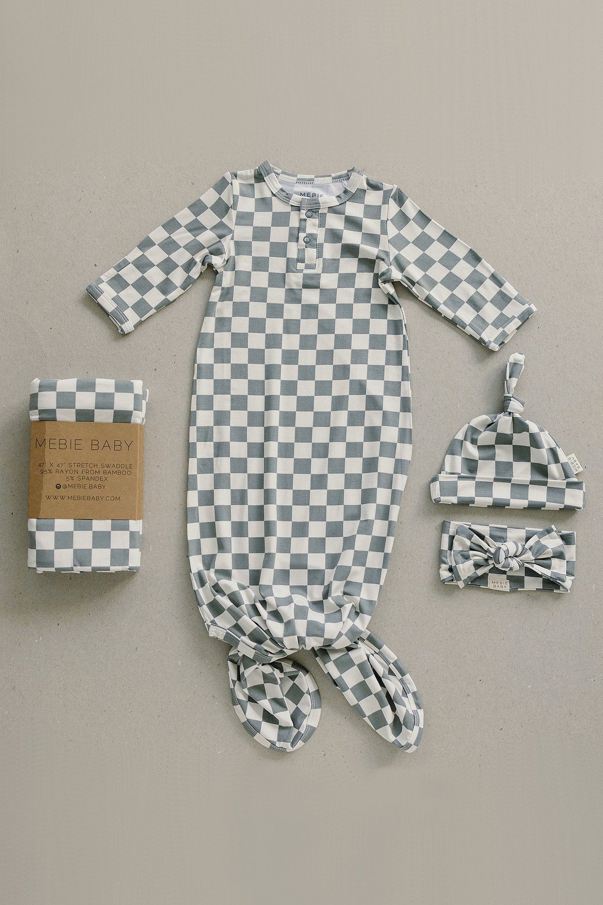 Checkered baby outfit set including a gown, hat, and headband, made from bamboo fabric, displayed on beige background.