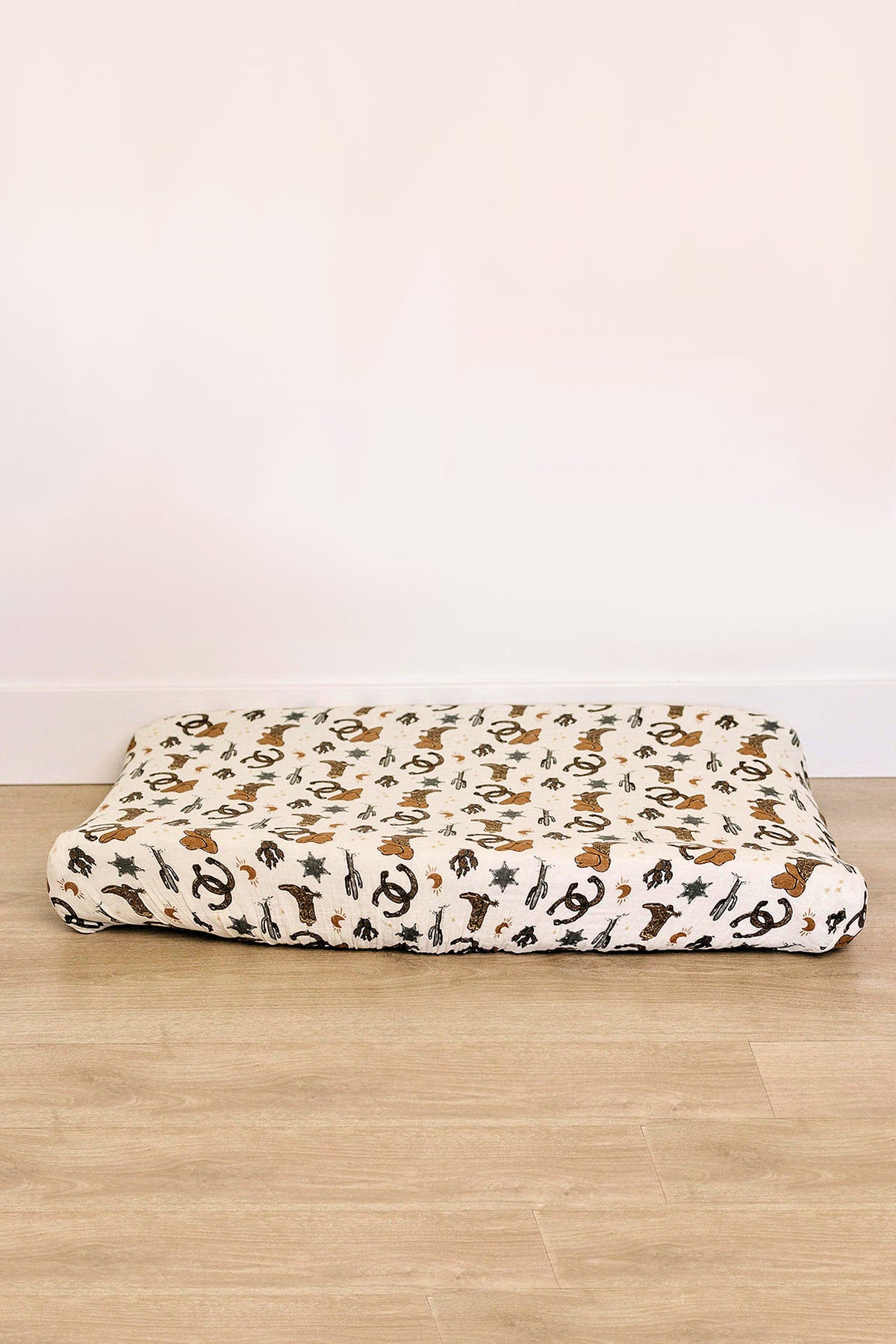 A muslin changing pad cover featuring a playful cowboy design in earthy tones. Made from 100% cotton, it offers a soft, breathable surface for babies.