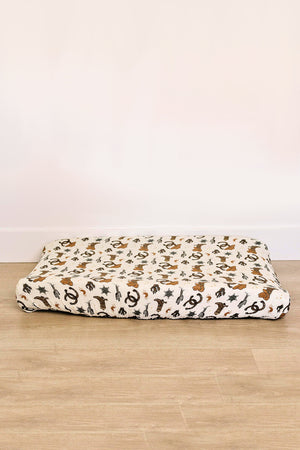 A muslin changing pad cover featuring a playful cowboy design in earthy tones. Made from 100% cotton, it offers a soft, breathable surface for babies.