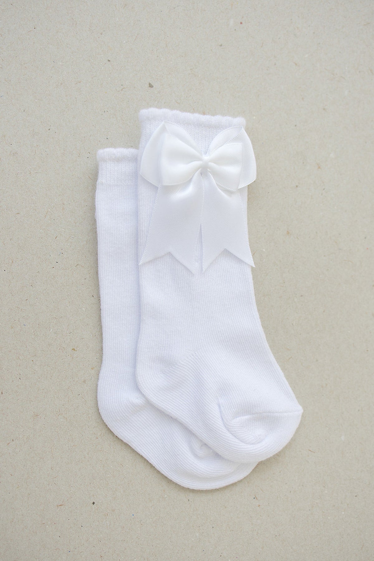 White cotton baby socks featuring a large satin bow, displayed on a neutral background.