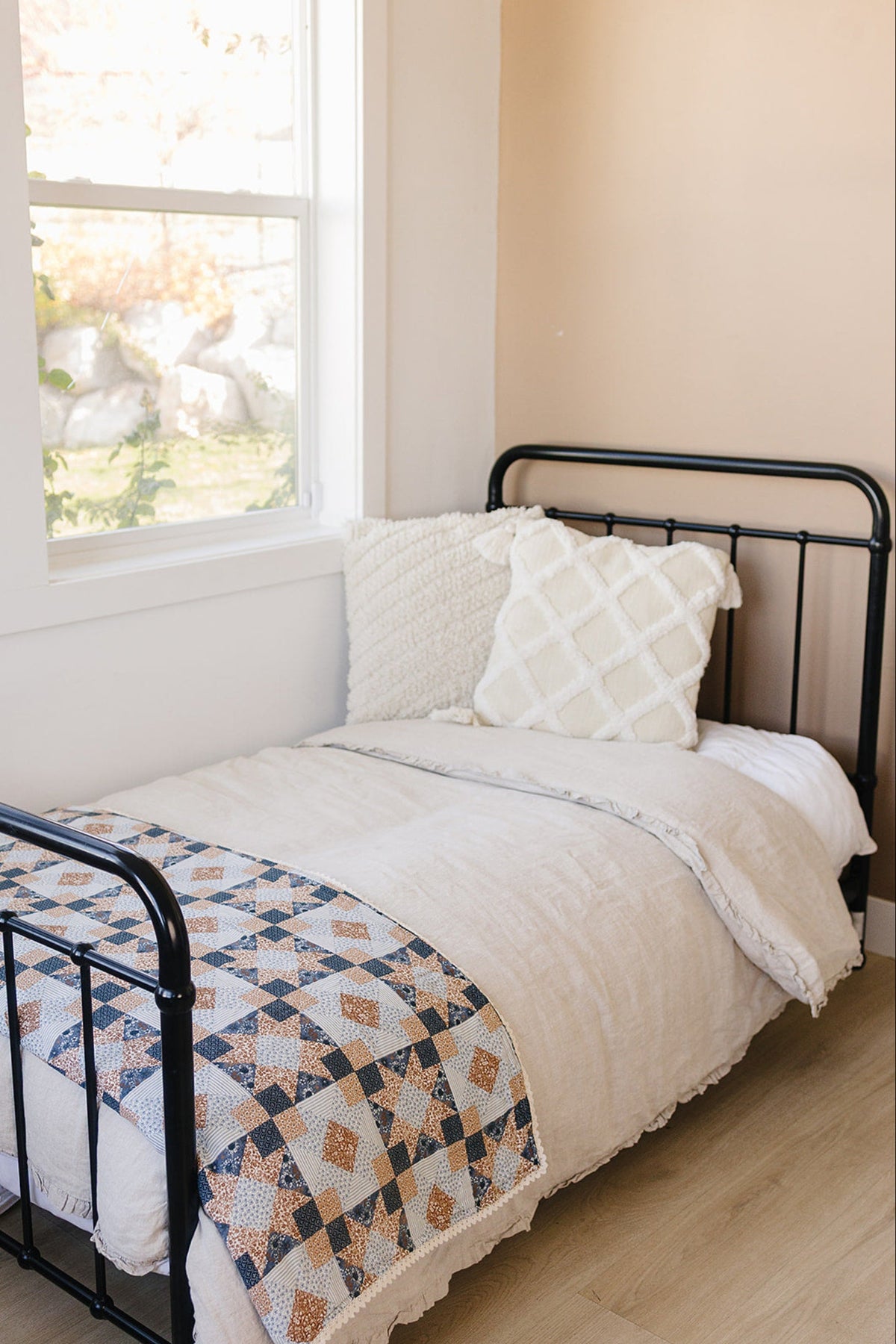 A cozy bed features a patchwork quilt with blue and orange patterns, paired with textured white pillows against a warm.