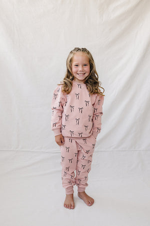 A smiling child wears a matching blush pink French terry cotton set adorned with a playful bow print.