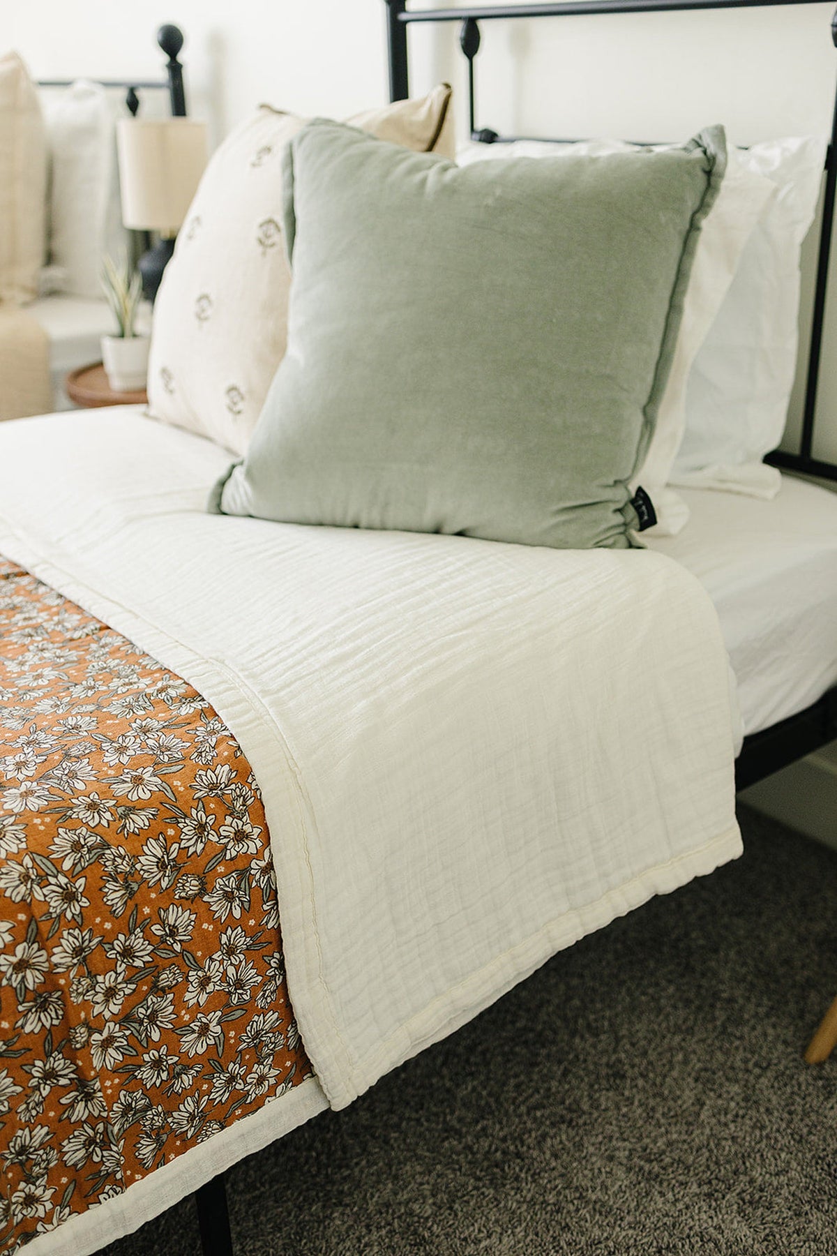 A cozy bed featuring a Magnolia floral muslin twin quilt in warm tones, complemented by soft pillows and a neutral.