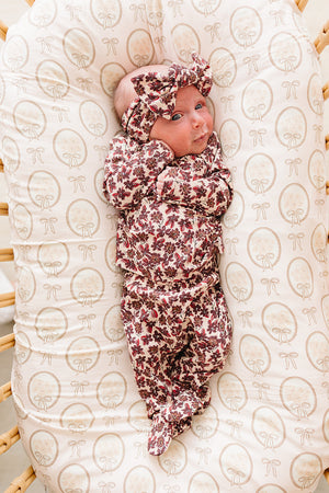 A baby lies comfortably on a floral-patterned, organic cotton mattress, wearing a matching ribbed bamboo layette set with a headband. The soft, breathable fabric is perfect for delicate skin.
