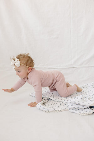 A baby crawls on a soft blanket, wearing a dusty pink waffle knit long sleeve bodysuit and matching pants.