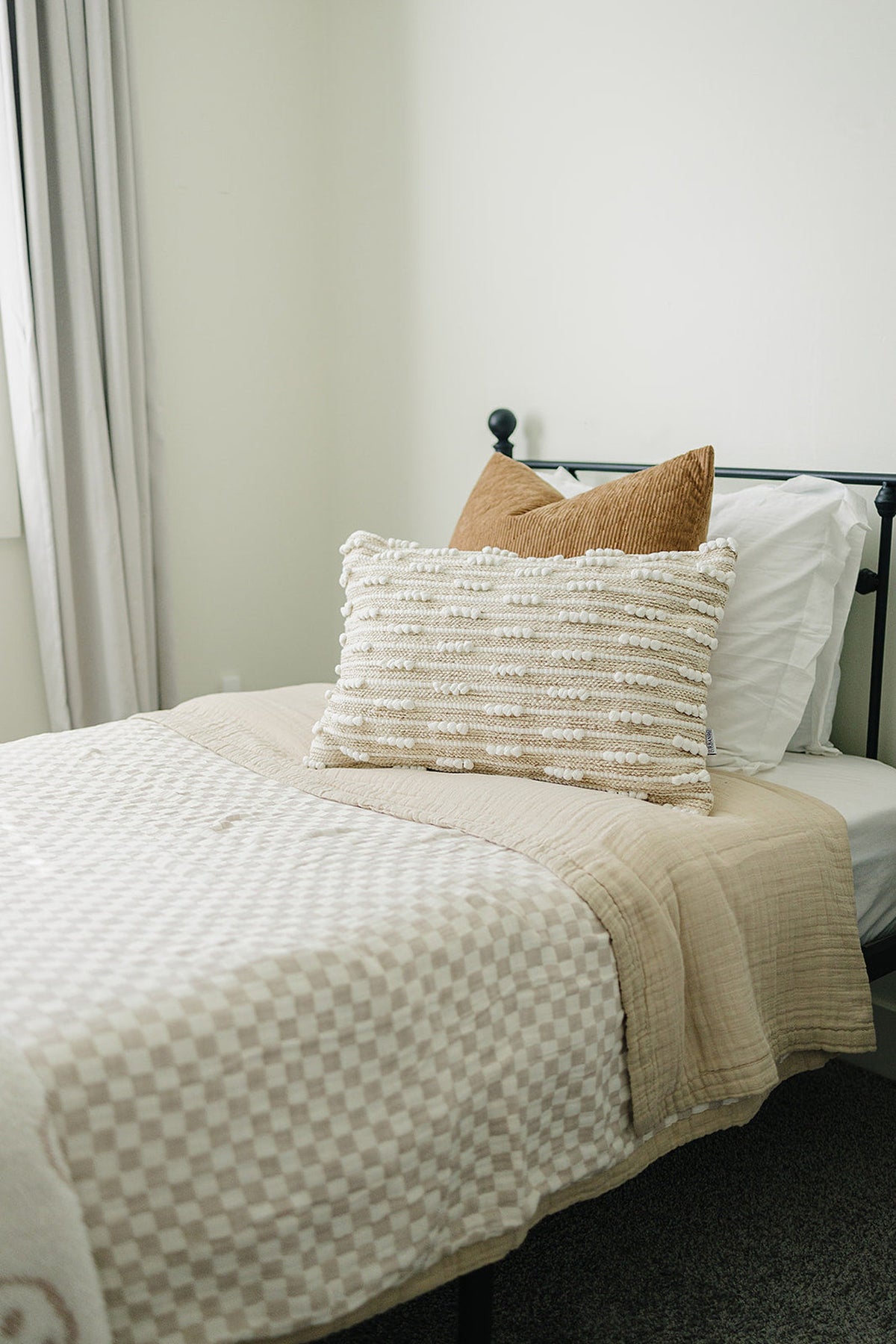 A taupe checkered quilt covers a bed with a textured pillow and brown cushion, creating a cozy look.