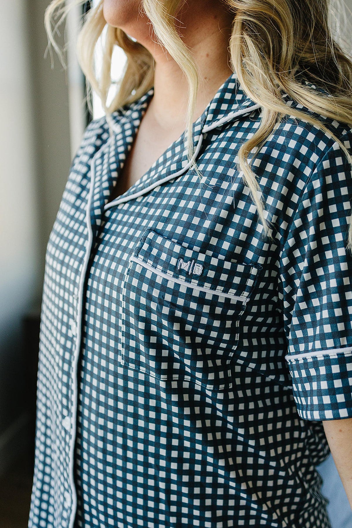 Close-up of a womans navy gingham pajama top with button-up design and embroidered initials MB on the pocket.