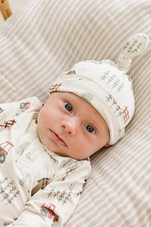 A baby lies on a striped crib mattress, wearing a soft, organic cotton outfit adorned with farm-themed prints.