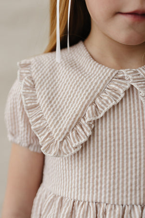 Close-up of a childs dress featuring a taupe striped pattern, a ruffled Peter Pan collar, and short puff sleeves.