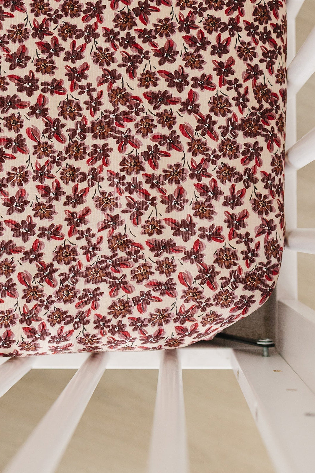 A close-up view of a crib sheet featuring a delicate floral pattern in shades of red and pink, crafted from soft, breathable bamboo fabric for comfort and sustainability.