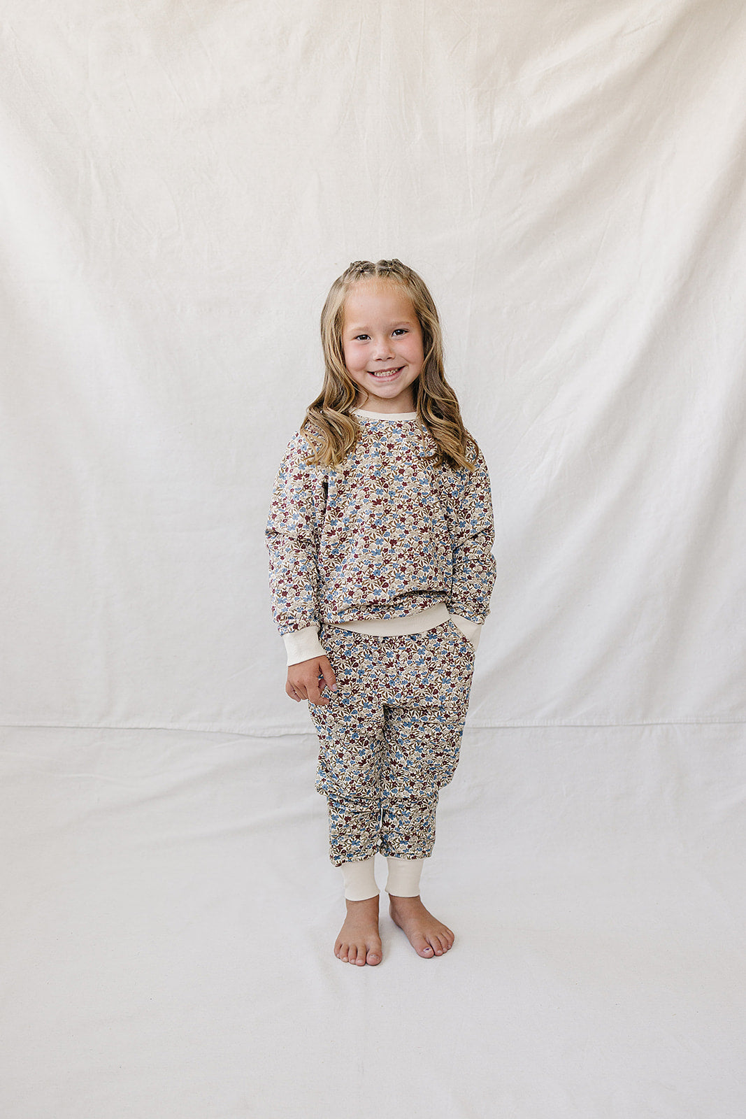 A young girl stands on a light backdrop, wearing a matching two-piece set featuring a colorful floral print. The soft, breathable fabric is perfect for comfort during playtime.