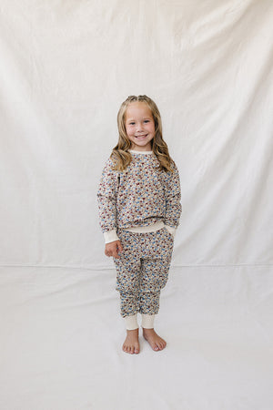 A young girl stands on a light backdrop, wearing a matching two-piece set featuring a colorful floral print. The soft, breathable fabric is perfect for comfort during playtime.