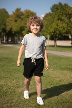 A child wearing a gray t-shirt and black shorts with white sneakers walks on grass in a sunny park.
