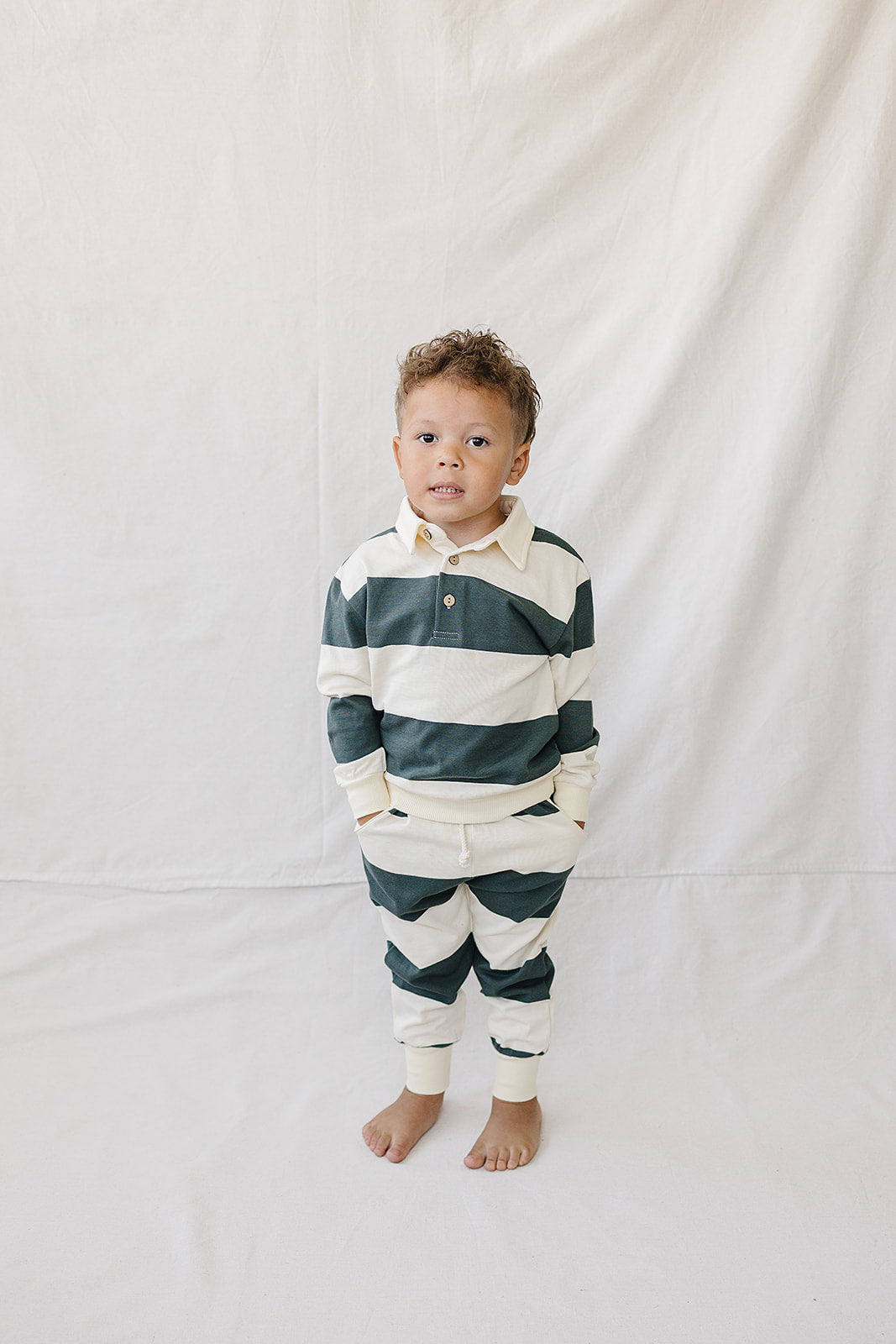 A young child stands wearing a green and white striped collared French terry cotton set. The outfit features a relaxed fit, perfect for everyday wear and comfort.