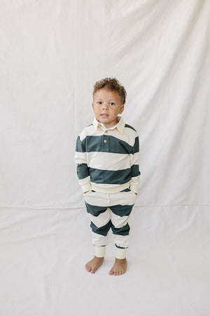 A young child stands wearing a green and white striped collared French terry cotton set. The outfit features a relaxed fit, perfect for everyday wear and comfort.
